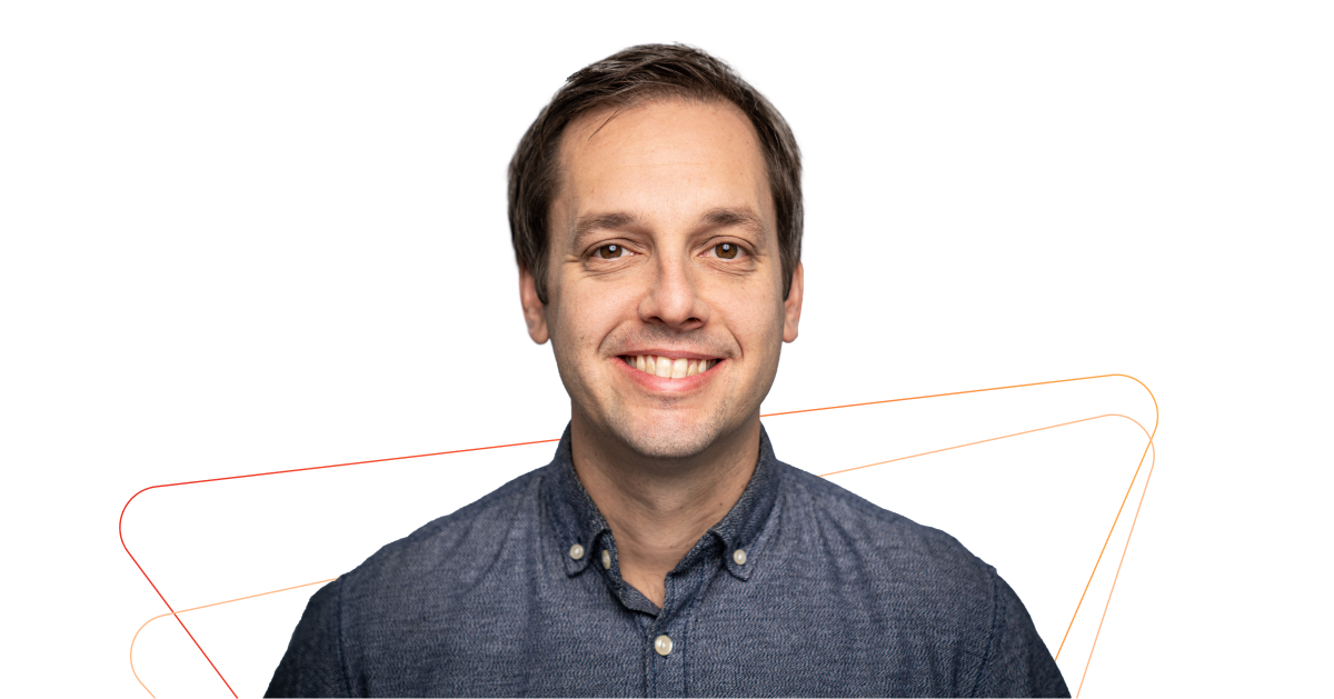 A man in a blue shirt is smiling in front of an orange triangle.