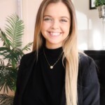 Abby Whalen, a smiling woman in a black blazer, sitting at a desk.