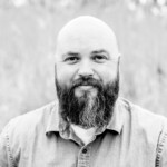 A black and white photo of a bald man with a beard named Alex Edwards.