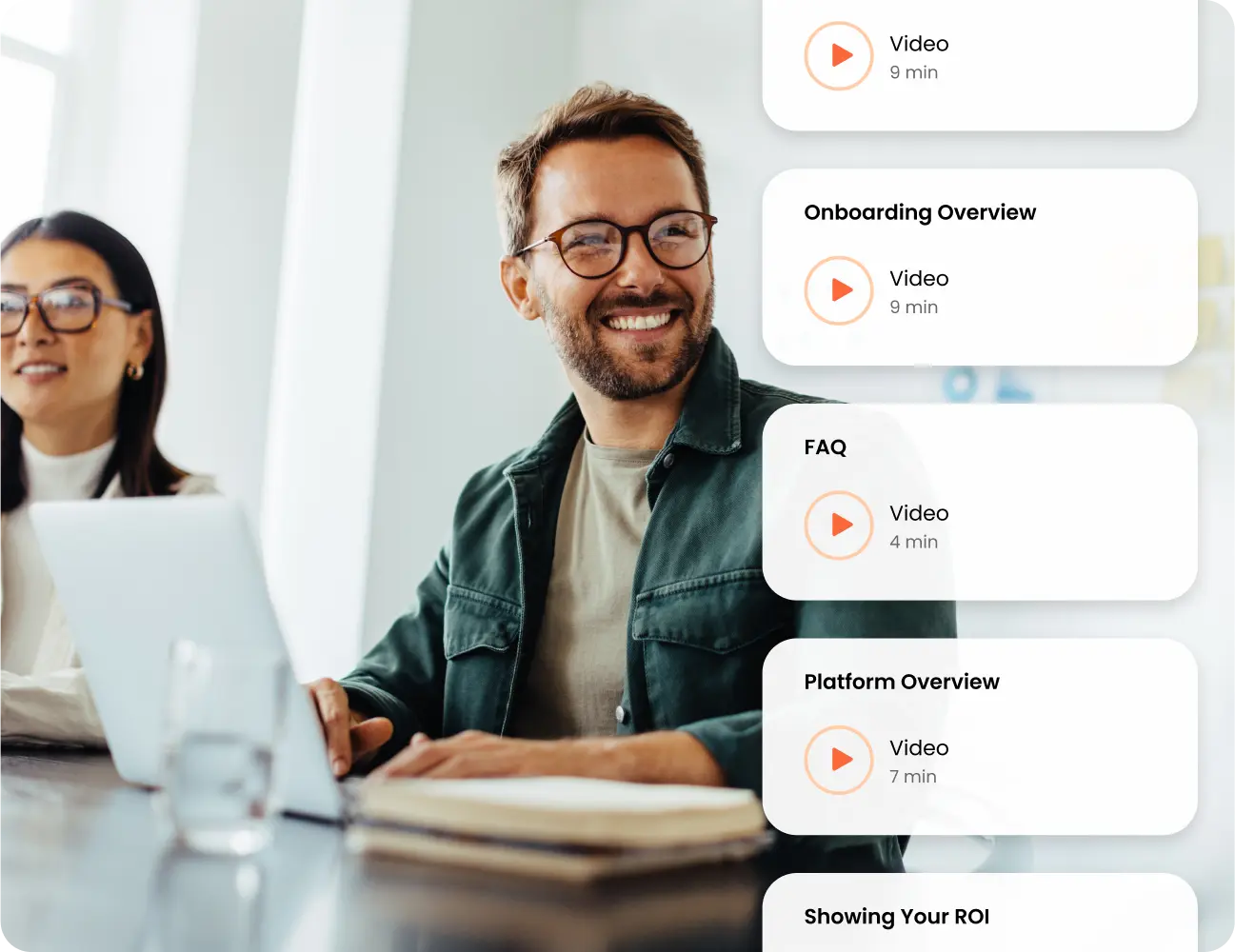 Two people are at a meeting table with laptops. The man in the foreground is smiling. The sidebar displays video titles: Onboarding Overview (9 min), FAQ (4 min), Platform Overview (7 min), and Showing Your ROI by Consensus Academy.