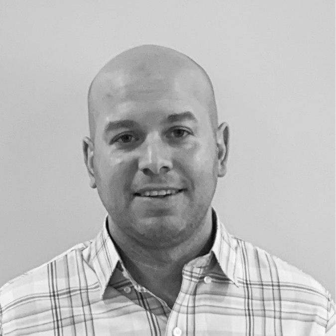 A bald man wearing a plaid shirt smiles at the camera against a plain background. Consensus