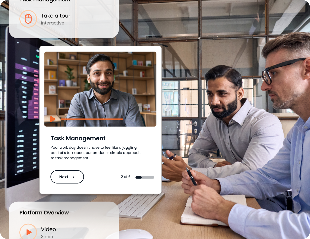 Three people in an office setting are discussing task management software, with a computer screen displaying details about the software. One man is smiling on the screen as part of a product demo, showcasing features integrated with Highspot for enhanced productivity.