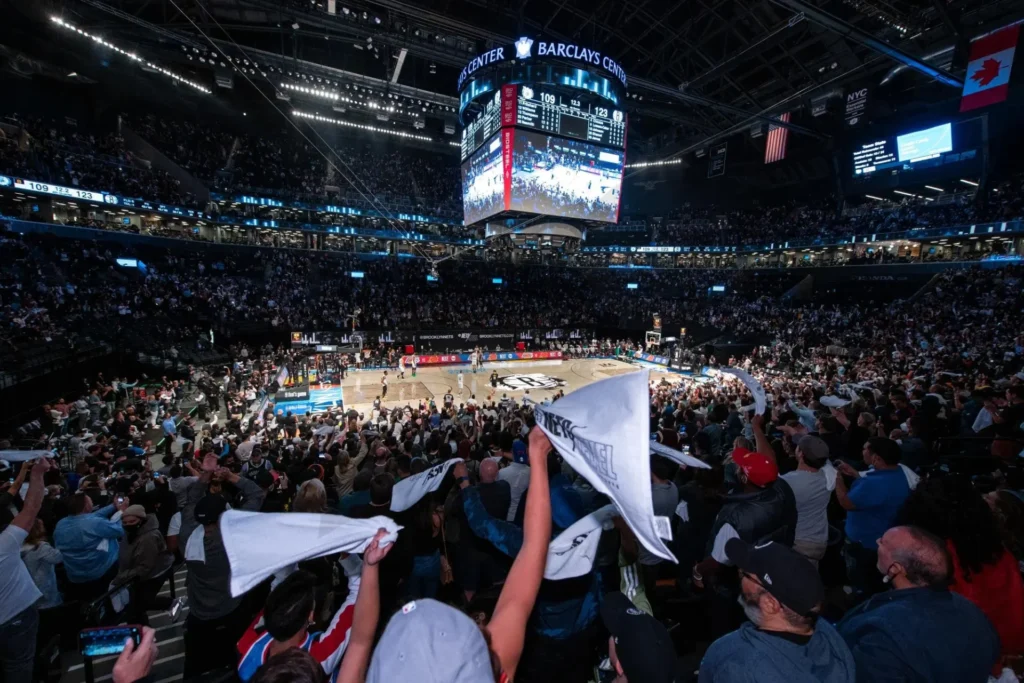 The packed arena buzzes with excitement as the Brooklyn Nets take on the Detroit Pistons. Fans are in consensus, waving towels energetically in the stands while the scoreboard hangs above, tracking every thrilling moment of the game.