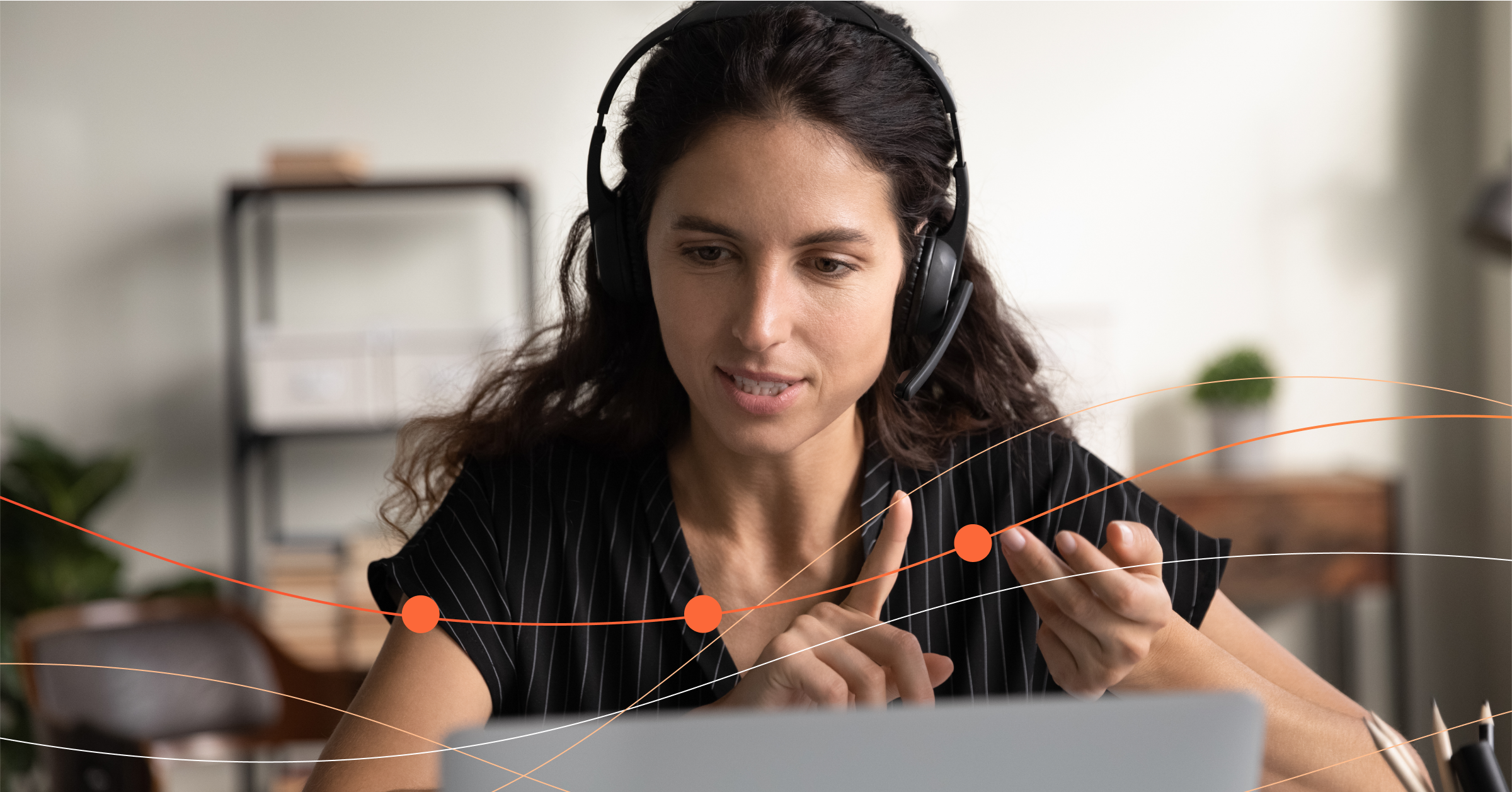 A focused woman wearing headphones participates in a virtual meeting, presenting a straightforward argument while gesturing and looking at her laptop screen.