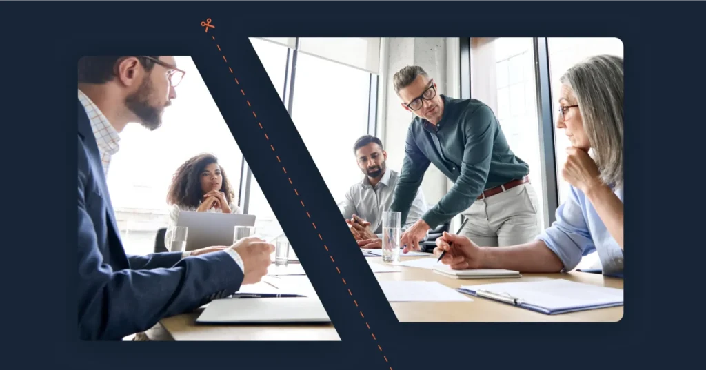 A group of people in the sales and marketing division gathers in a meeting room, engaging in discussion around a table with notes and glasses of water. One person stands, gesturing passionately, while others sit listening intently and taking notes. Consensus