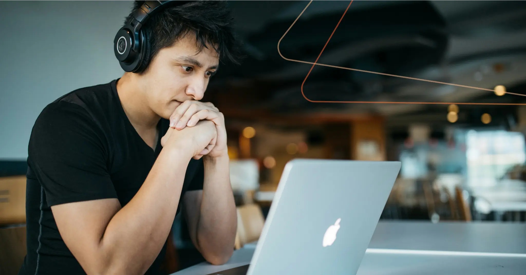 A person wearing headphones looks at a laptop screen with a focused expression, sitting at a table in a modern indoor setting, possibly reviewing data on sales team turnover.