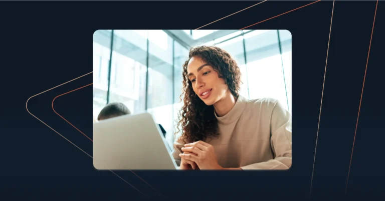 A woman with curly hair sits at a desk, looking at a laptop screen in a bright, modern office space—perfect for Revenue Teams aiming to Sell in the Gap. Consensus