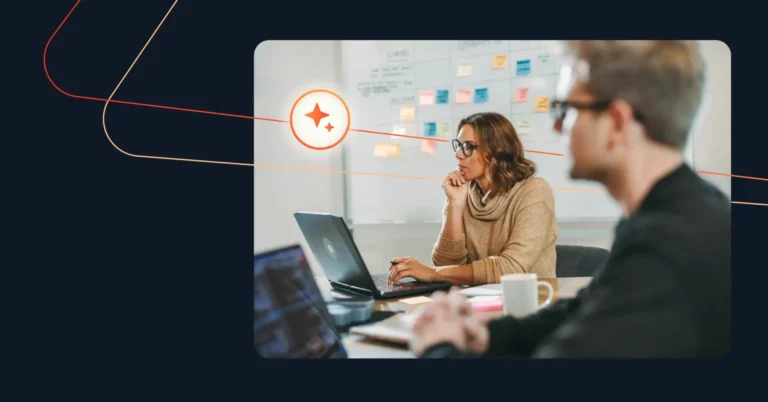 Two people working at a desk with laptops; one person is in focus, looking at a screen. Sticky notes on a whiteboard in the background hint at strategies to boost the sales process using AI innovations. Consensus