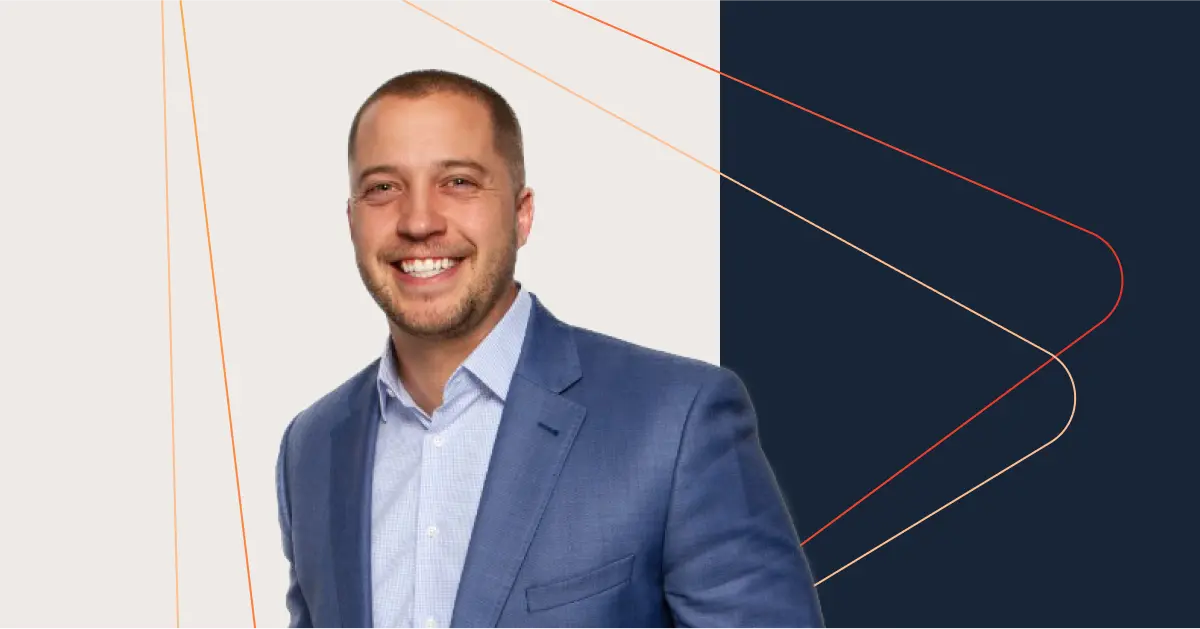 A man wearing a blue blazer and light blue shirt, embodying C-Suite elegance, smiles at the camera with a geometric background.